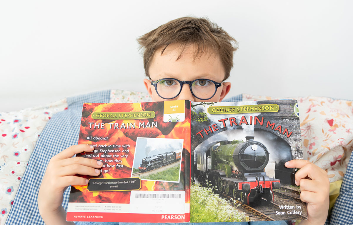 child in glasses reading book about trains